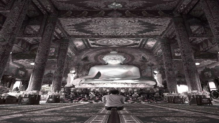 A boy is sitting and praying in front of the statue of God.